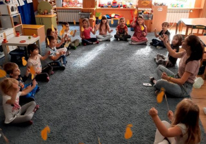 Dzieci siedzą na dywanie z nauczycielką rytmiki